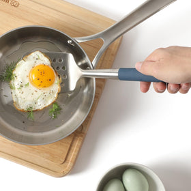 Calphalon Edge slotted turner in use over a pan during cooking.