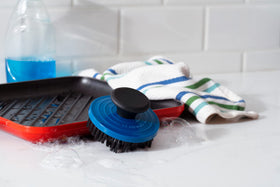 Le Creuset grill pan brush in use demonstrates safe cleaning between ridges.