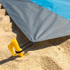 Oualhoo stakes securing a beach blanket on a windy shore