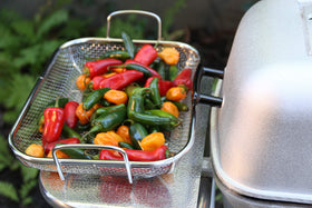 Outset stainless steel grill roasting basket on a hot grill, veggies retained