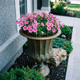 Worth Garden urn planter by garden border enhances landscape with antique bronze appeal.